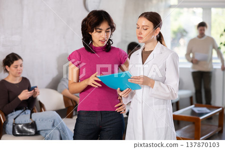 Malaysian woman standing at the reception and talking to a nurse Malaysian woman standing at the reception and talking to a nurse 137870103