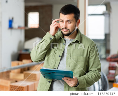 Architect making notes on indoor construction site 137870137