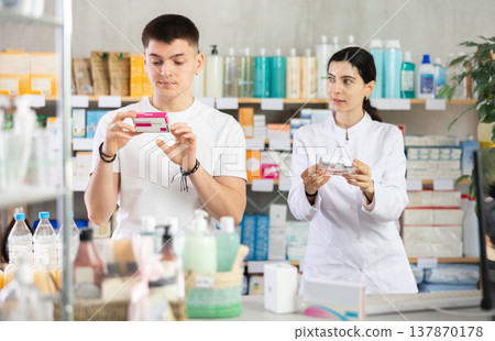 Young man buys pills at drug store, pharmacist in background Young man buys pills at drug store, pharmacist in background 137870178
