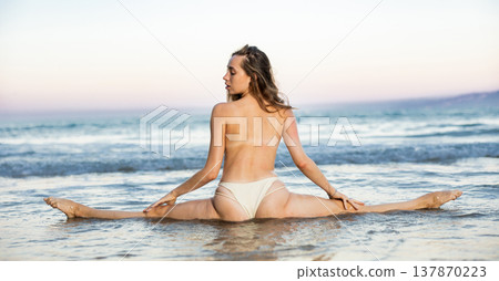Girl model doing splits, sitting in cross-split pose, rear view 137870223