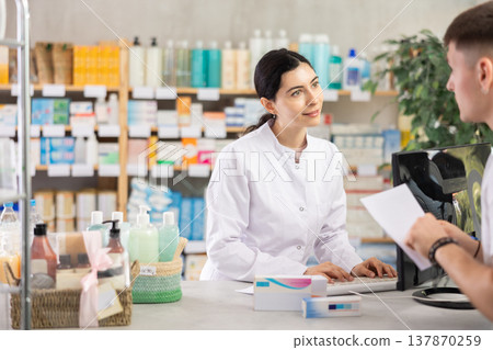 Girl pharmacist at counter with computer sells pills, consulting guy about doctors prescription. 137870259