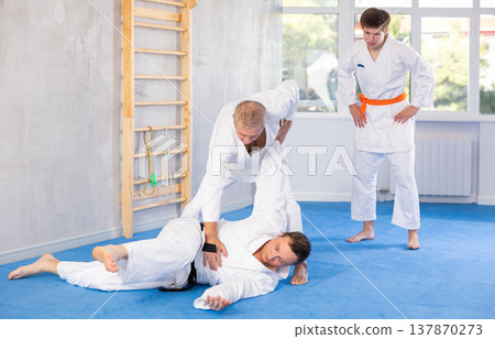 Judo or jiu jitsu classes - two men of different age practicing grabbing and throwing on sports mats Judo or jiu jitsu classes - two men of different age practicing grabbing and throwing on sports mats 137870273