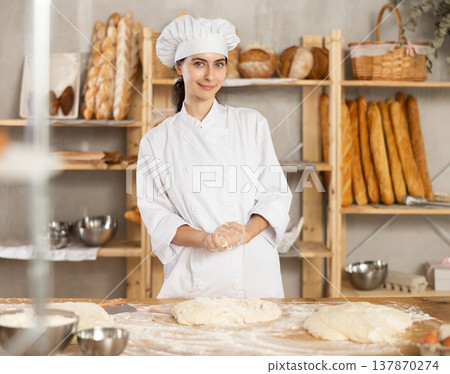 Young woman works in bakery as baker, kneads dough, works with flour. Young woman works in bakery as baker, kneads dough, works with flour. 137870274