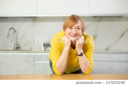 Happy older lady standing in kitchen with warm smile 137870290
