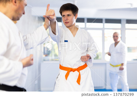 Young guy and his coach practice punches in karate sparring in gym Young guy and his coach practice punches in karate sparring in gym 137870299