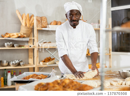 Passionate African baker kneading dough on floured table Passionate African baker kneading dough on floured table 137870308