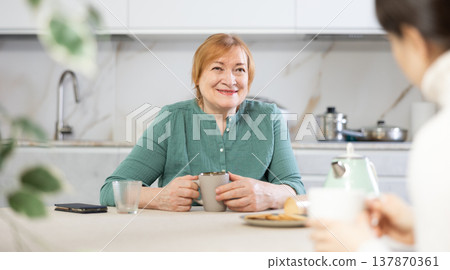 Friendly mature woman and a female guest drink tea together and talk 137870361