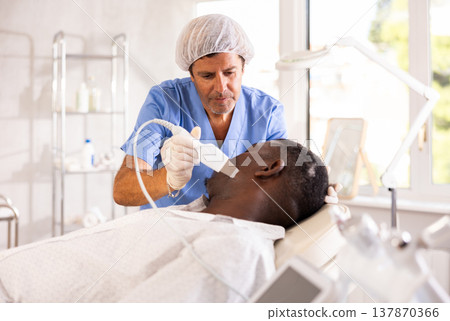 Cosmetologist performing facial cleansing with ultrasonic shovel on black man Cosmetologist performing facial cleansing with ultrasonic shovel on black man 137870366