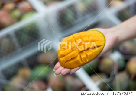 Fresh sliced mango on hand, blurred boxes with fruits on background Fresh sliced mango on hand, blurred boxes with fruits on background 137870374