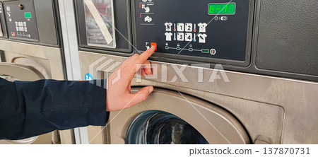 A man presses a button on the control panel of a washing machine at a self-service laundromat. Concepts of everyday life, automation, household services, and the use of modern household appliances 137870731
