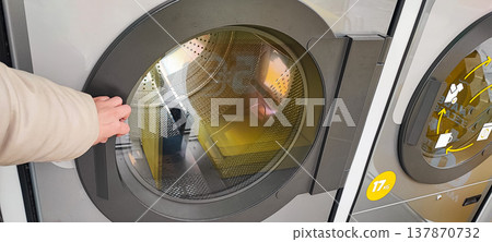 A man presses a button on the control panel of a washing machine at a self-service laundromat. Concepts of everyday life, automation, household services, and the use of modern household appliances A man presses a button on the control panel of a washing machine at a self-service laundromat. Concepts of everyday life, automation, household services, and the use of modern household appliances 137870732