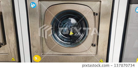 A man presses a button on the control panel of a washing machine at a self-service laundromat. Concepts of everyday life, automation, household services, and the use of modern household appliances A man presses a button on the control panel of a washing machine at a self-service laundromat. Concepts of everyday life, automation, household services, and the use of modern household appliances 137870734