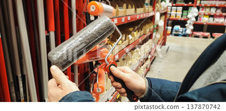 A customer holds a paint tray and brushes while shopping in a hardware store aisle. Concepts of home improvement, DIY renovation, consumer choice, and retail shopping behavior. A customer holds a paint tray and brushes while shopping in a hardware store aisle. Concepts of home improvement, DIY renovation, consumer choice, and retail shopping behavior. 137870742
