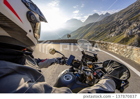 Motorcycle rider riding in Italian Alps during sunrise , handlebar view , dramatic sky . Travel and freedom, outdoor activities Motorcycle rider riding in Italian Alps during sunrise , handlebar view , dramatic sky . Travel and freedom, outdoor activities 137870837