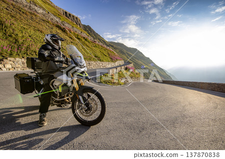 Motorcycle rider posing in Italian Alps during sunrise, dramatic sky. Travel and freedom, outdoor activities Motorcycle rider posing in Italian Alps during sunrise, dramatic sky. Travel and freedom, outdoor activities 137870838