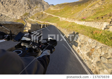 Motorcycle rider riding in Italian Alps during sunrise , handlebar view , dramatic sky . Travel and freedom, outdoor activities Motorcycle rider riding in Italian Alps during sunrise , handlebar view , dramatic sky . Travel and freedom, outdoor activities 137870839