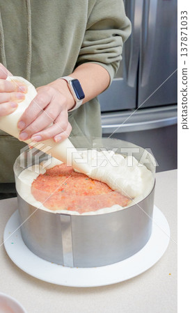 Person decorating a layered cake with cream frosting using a piping bag in a modern kitchen setting with stainless steel appliances Person decorating a layered cake with cream frosting using a piping bag in a modern kitchen setting with stainless steel appliances 137871033