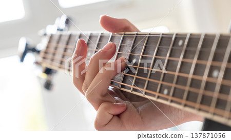 Close-up of a hand playing guitar strings, showcasing finger placement and wooden fretboard in a bright indoor setting with natural light Close-up of a hand playing guitar strings, showcasing finger placement and wooden fretboard in a bright indoor setting with natural light 137871056