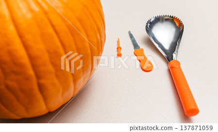 Orange pumpkin with carving tools including a scoop and knife on a light surface, ready for Halloween decoration and festivities 137871059