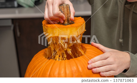 Person cutting open a pumpkin for Halloween preparation, revealing seeds and pulp inside, with kitchen countertop visible in the background 137871063