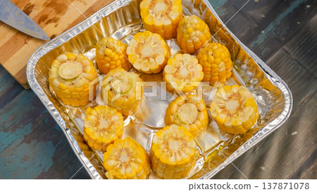 Freshly cut yellow corn cobs arranged in a silver aluminum tray on a rustic wooden surface with a knife nearby Freshly cut yellow corn cobs arranged in a silver aluminum tray on a rustic wooden surface with a knife nearby 137871078