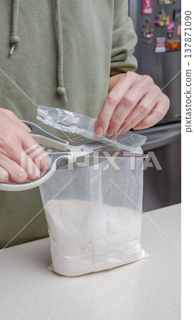 Person using scissors to open a plastic bag containing white powder on a kitchen countertop with a refrigerator in the background Person using scissors to open a plastic bag containing white powder on a kitchen countertop with a refrigerator in the background 137871090