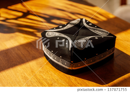 Elegant Cultural Accessory. Sunlit Kufi With Intricate Silver Needlework On Wooden Surface 137871755