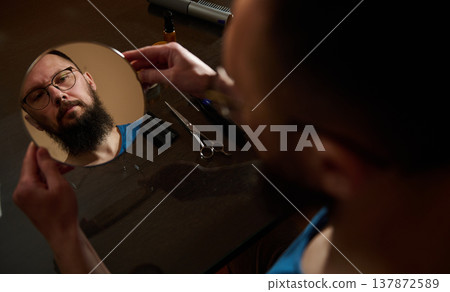 Man Inspecting Beard in Handheld Mirror While Preparing to Trim at Home Man Inspecting Beard in Handheld Mirror While Preparing to Trim at Home 137872589