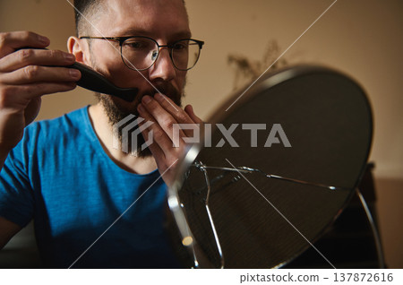 Man Grooming Beard With Electric Trimmer While Checking Face In Mirror Man Grooming Beard With Electric Trimmer While Checking Face In Mirror 137872616