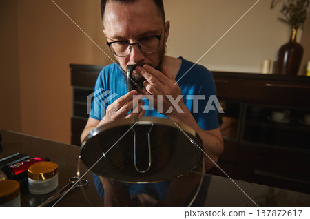 Man Trimming Nose Hair in Mirror at Home Grooming Table With Trimmer and Scissors Man Trimming Nose Hair in Mirror at Home Grooming Table With Trimmer and Scissors 137872617
