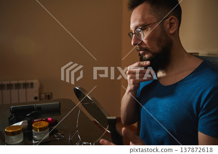 Man Grooming Beard in Mirror at Home With Glasses and Trimmer on Table Man Grooming Beard in Mirror at Home With Glasses and Trimmer on Table 137872618