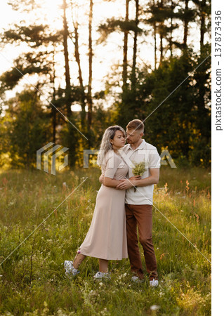 Young couple embracing in meadow at sunset with forest background 137873436