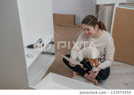 A Caucasian woman assembles furniture with her cute dog. 137873450