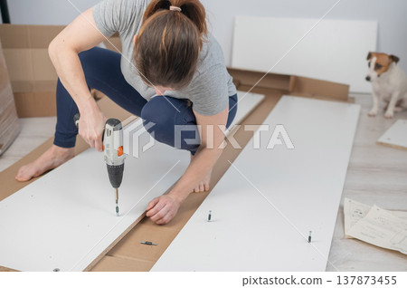 A Caucasian woman uses a screwdriver to tighten a screw while assembling a cabinet. 137873455