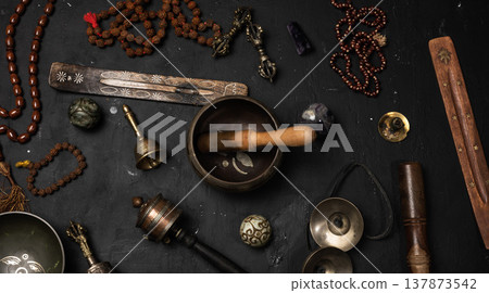 Tibetan singing bowl, wooden resonator, ritual vajras, bell, prayer wheel, rosary beads, and incense on a black background Tibetan singing bowl, wooden resonator, ritual vajras, bell, prayer wheel, rosary beads, and incense on a black background 137873542
