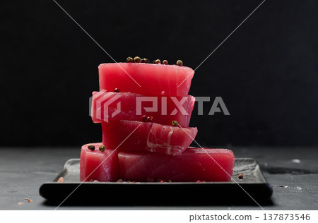 Stack of raw tuna pieces on black plate, black table Stack of raw tuna pieces on black plate, black table 137873546