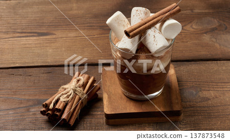 A glass of hot chocolate or cocoa with lots of cinnamon-dusted marshmallows on a wooden background. A cozy winter drink. 137873548