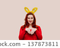 Young red-haired woman in red dress wearing easter costume with bunny ears. 137873811
