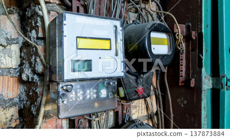 Old analog electricity meter stands next to a modern digital one in a dilapidated interior. Old analog electricity meter stands next to a modern digital one in a dilapidated interior. 137873884