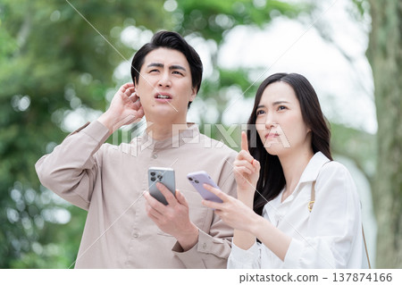 A couple looking at their smartphones outdoors. A couple looking at their smartphones outdoors. 137874166
