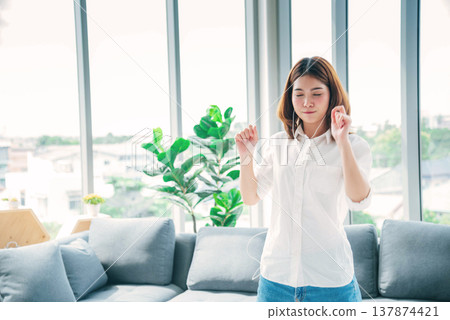 Happy asian dancing woman use headphones listen to music from smartphone happy dance in living room at home. Music mental therapist relaxation woman. Cheerful wellness women dance exercise wellbeing 137874421
