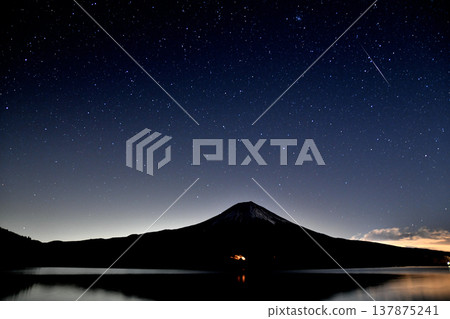 A meteor from the Geminid meteor shower, seen streaking across Mount Fuji from Lake Tanuki in Fujinomiya City, Shizuoka Prefecture. 137875241