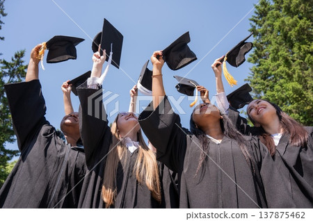 Young women of different nationalities pull graduation caps up.  137875462