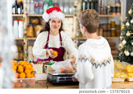 Woman sells fruits to teen boy, puts tangerines in bag, puts them on scale and weighs fruits Woman sells fruits to teen boy, puts tangerines in bag, puts them on scale and weighs fruits 137878028