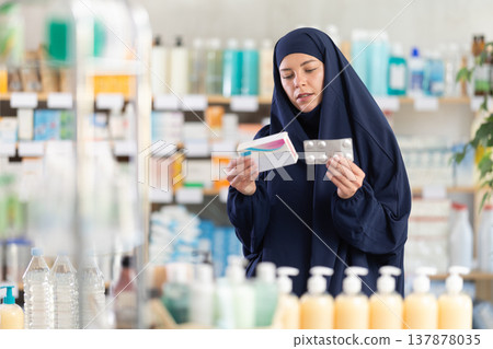 Young woman in khimar examining medicine box at pharmacy 137878035