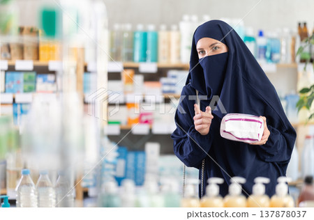 Young woman in Muslim attire choosing feminine pads in pharmacy Young woman in Muslim attire choosing feminine pads in pharmacy 137878037