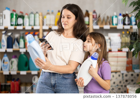Mother and daughter checking expiration date of detergent using her smartphone in supermarket Mother and daughter checking expiration date of detergent using her smartphone in supermarket 137878056