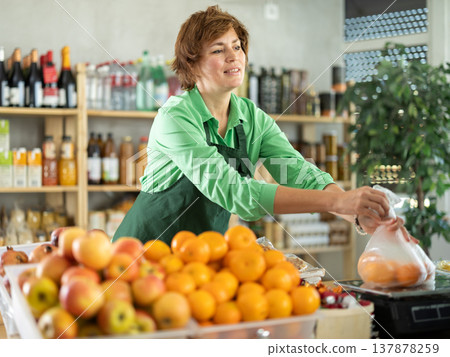 Female employee sells fruits, take out bag with tangerine, puts them on scale and weighs fruits Female employee sells fruits, take out bag with tangerine, puts them on scale and weighs fruits 137878259