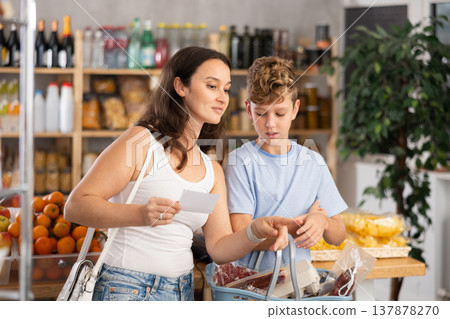 Mother and teenage son chooses products from checklist on paper in supermarket Mother and teenage son chooses products from checklist on paper in supermarket 137878270