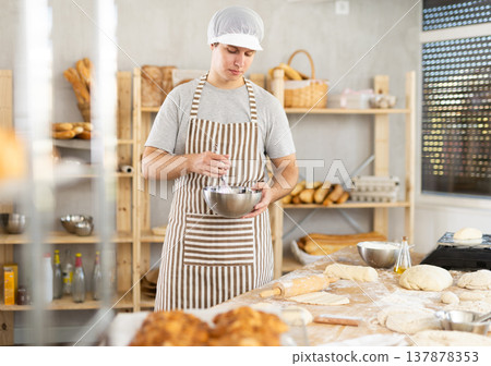 Young male baker whipping dough in bowl Young male baker whipping dough in bowl 137878353